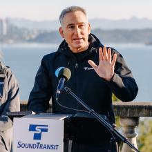 Dow Constantine speaking outside with microphone, with Sound Transit logo visible.