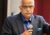 Aseem Prakash in a suit, holding a microphone